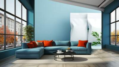 A minimalistic display of two white packaging bags beside a green plant against a soft blue background, emphasizing simplicity and freshness. Wall mural