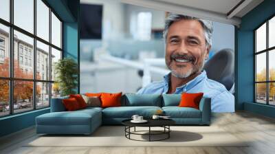 a happy middle aged man in blue shirt at a bright dentist office relaxed in the orthodontic dental chair smiling while getting teeth cleaned and repaired Wall mural