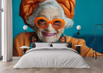 Joyful elderly woman in vibrant colorful clothing with bright orange sunglasses, laughing and smiling, playful granny posing in studio with extravagant style and trendy neon outfit Wall mural