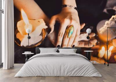 close-up portrait of young beautiful red-haired girl in the image of a Gothic witch on Halloween on a background of wax candles, fire, magic crystals and stones in the black dress conjures Wall mural