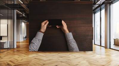 Accountant student hands hold smart phone horizontally, readind news, wearing his classic silver watches with leather strap and plaid shirt. Isolated on red wooden table in meeting room, top view Wall mural