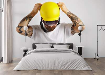 attractive tattooed and bearded young snowboarder wearing plain white t-shirt and yellow helmet putt Wall mural