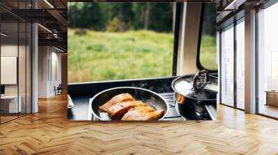 Close up on frying pan with organic salmon prepared in inside camper van on campsite in mountains or forest. Life on the road, camper van lifestyle outdoors vibes. Prepare food in converted vehicle Wall mural