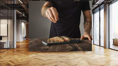 Man cooks healthy meal on rustic wooden table, salts two raw pieces of salmon in white wine sause with spices and herbs presented on marble deck prepared for grill  Wall mural