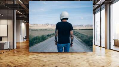 Photo from the back of brutal masculine man with authentic arm tattoos in blank black mockup tshirt standing in middle of desert highway Wall mural