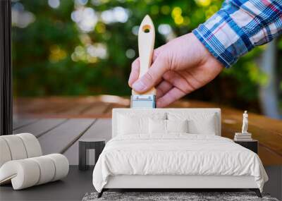 a hand holding a brush applying varnish paint on a wooden garden table - painting and caring for wood with oil Wall mural