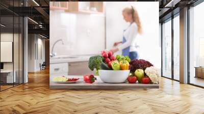 Fresh vegetables on table with woman in background Wall mural