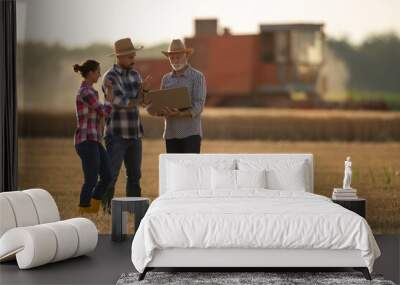 Three farmers with laptop talking in field during harvest Wall mural