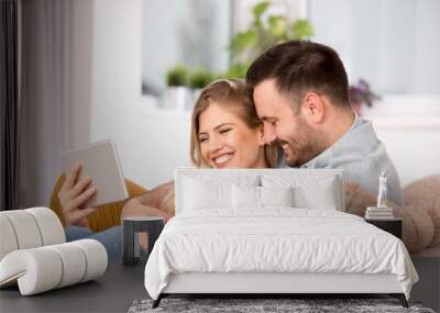 Young couple looking at tablet and laughing at home Wall mural