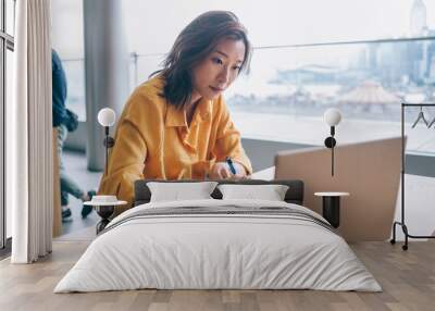 Asian female writing and looking at screen display at workplace Wall mural