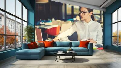 Attractive female economist in elegant outfit checking documentation and reports of restaurant incomes working with online database making statistics and amount of costs using modern technologies Wall mural