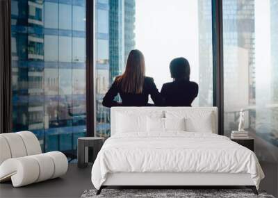 Back view of female colleagues in formal wear standing near window looking at modern exterior of skyscrapers in business center, prosperous women standing together planning prosperous future success Wall mural