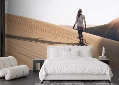 Back view of female wanderer exploring wild Sahara desert during summer evening with sunrise time in nature environment, woman tourist walking in sands wilderness discovering breathtaking Safari Wall mural