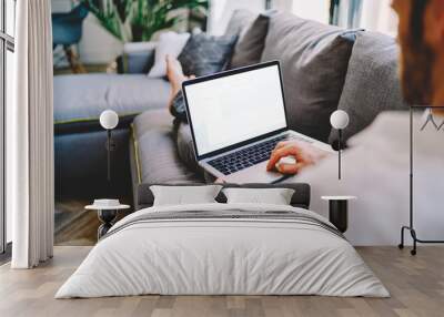 Back view of skilled man taking rest on couch with laptop computer with mock up screen for your internet advertising, male blogger publishing new article on content website using 4g wireless Wall mural