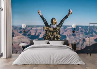 Back view of young wanderlust feeling victory conquering mountain in Grand Canyon, female traveler with backpack raising hands enjoying beautiful nature from high rocky hills getting to destination Wall mural