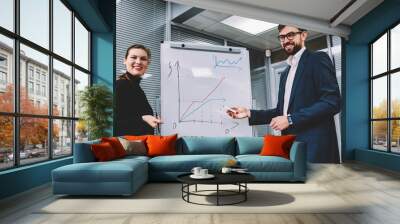 Beautiful businesswoman with smart assistant giving presentation to colleagues in meeting, people talking about new office  explaining benefits on flip chart graphs showing why it is great idea Wall mural