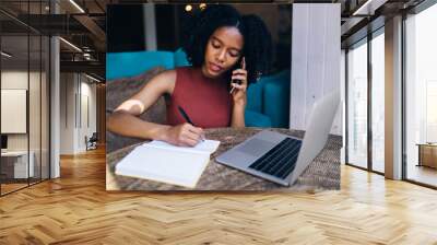 Black careful remote worker writing in notebook talking to colleague in cafeteria Wall mural