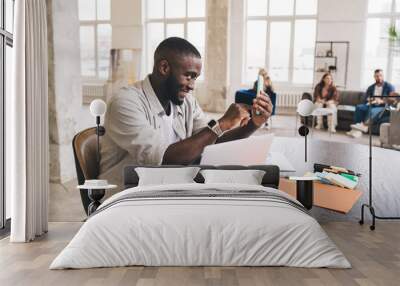 Black man using smartphone while working on laptop Wall mural