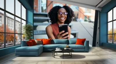 Cheerful black female using cellphone spending time in street Wall mural