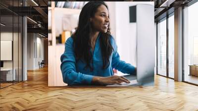 Cheerful black manager typing checking information on monitor at table Wall mural