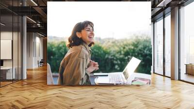 Cheerful digital nomad at table with laptop Wall mural