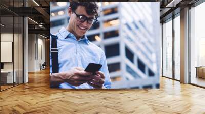 Cheerful man browsing smartphone on street Wall mural