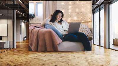 Cheerful woman browsing laptop on sofa Wall mural