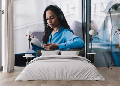 Concentrated ethnic woman using tablet on couch Wall mural