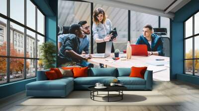 Concentrated female manager showing to employees digital information on smartphone, young colleagues reading news in social network while having meeting in office interior sitting together at table Wall mural