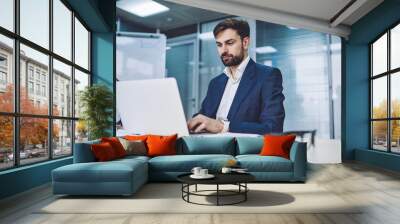 Concentrated male lawyer in formal wear booking tickets on website while using modern laptop device with wireless internet connection in conference room, concept of business people and technology Wall mural