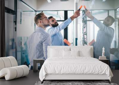 Confident male employee pointing on notes standing with colleague near glass creating infographic for conversation, skilled managers discussing sketches and planning during informal meeting in office Wall mural