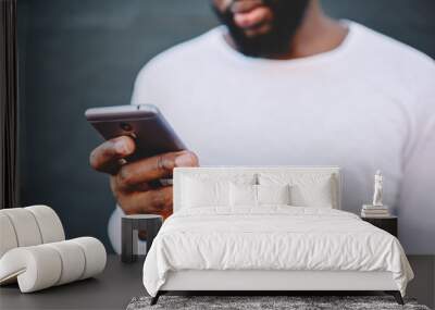 Cropped image of african american man holding modern smartphone dialing number, dark skinned male in white shirt using mobile phone for chatting in social networks via 4G internet connection outdoors Wall mural