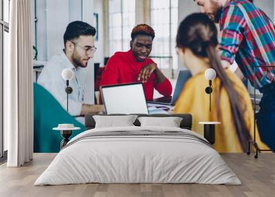 Diverse people discussing creative ideas for new project teamworking at meeting table using mockup netbook with blank screen, youthful male and female designers cooperating during together briefing Wall mural