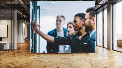 Diverse team of skilled students together solving task writing down information on papers glued on wall.Multicultural young people collaborating on business plan making notes of ideas on sticker Wall mural