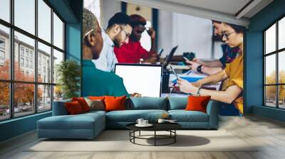 Diversity group of male and female employees using laptop computers suring working process on project, skilled colleagues using modern technology and wifi connection in office during meeting table . Wall mural