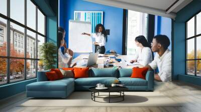 Enthusiastic ethnic businesswoman doing presentation for multiethnic coworkers at conference room Wall mural