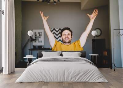 Excited man with raised arms at home Wall mural