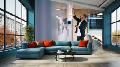 Focused man writing on glass board in office Wall mural