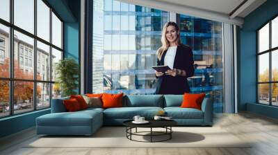 Half length portrait of Caucasian female entrepreneur with modern touch pad in hands smiling at camera posing in office interior, prosperous business woman in elegant suit holding digital tablet Wall mural