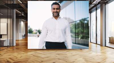 Half length portrait of cheerful businessman 40 years old dressed in white shirt smiling at camera in financial district, happy Caucasian male employer in formal clothes posing in city downtown Wall mural