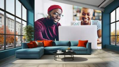 Happy dark skinned male and female watching video on laptop computer sitting at apartment, positive couple of african american hipsters having conversation while share photos in social networks Wall mural