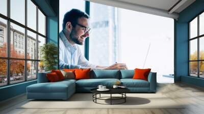 Happy male executive manager in glasses for vision protection enjoying online marketing on trade website connecting to office internet for browsing, cheerful financial expert using digital technology Wall mural