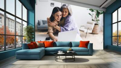 Happy mother embracing daughter using laptop in living room Wall mural