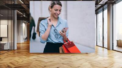 Happy woman using smartphone for sending text messages chatting via modern application, female customer with packages sharing publication about Black Friday sales in personal fashion web blog Wall mural