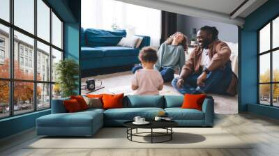 Joyful young diverse parents with little child sitting on floor at home Wall mural