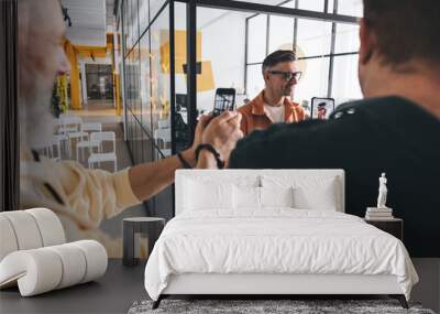 Male colleagues taking picture of standing adult man in eyeglasses at workplace Wall mural