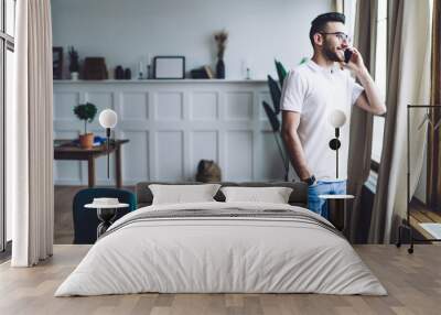 Man looking out window and talking on phone at home Wall mural