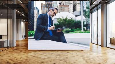 Mature businessman using tablet with stylus pen on city street Wall mural