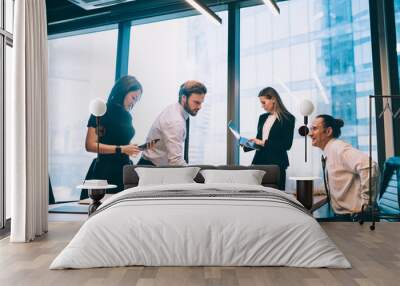 Mature male office workers dressed in suits discussing ideas and opinions about financial startup project while business women sharing information via cellular and laptop devices using bluetooth Wall mural