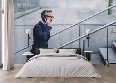 Middle-aged businessman talking by smartphone on urban background Wall mural